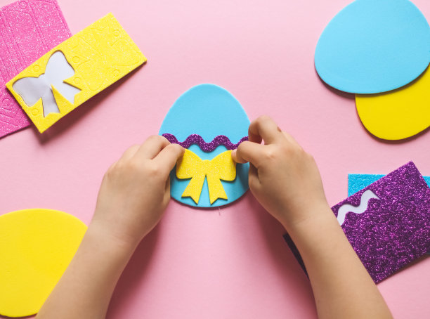 一个白人小女孩的手把黄色的蝴蝶结贴在一个毛毡蛋上图片下载