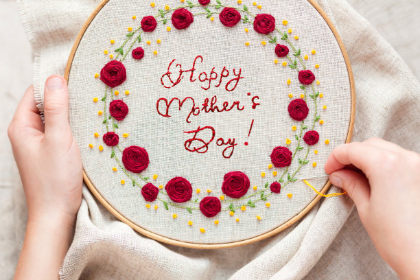 “母亲节快乐”的铭文被绣在织物上的一个花框里。图片下载