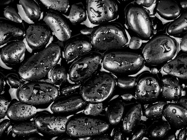 黑色的河石纹理和背景。黑色的鹅卵石在水中和水滴。图片下载