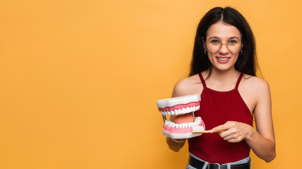 一张黄色背景的照片上，一位有着健康牙齿的微笑女性正用牙刷清洁着下颚的形状。口腔卫生。一个发短信的地方。图片下载