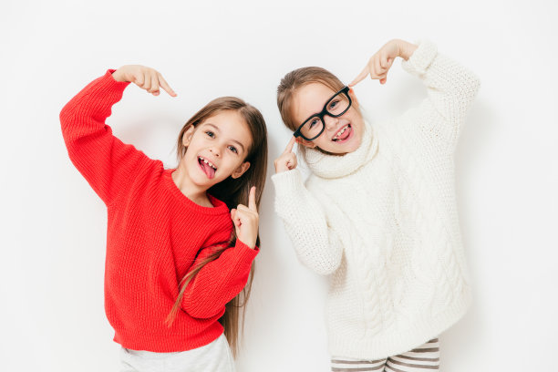 心情愉快的女生，穿着超大毛衣，戴着眼镜，做着酷炫的手势，在白色背景下一起摆姿势。快乐的女性孩子有乐趣。童年与幸福的概念图片下载