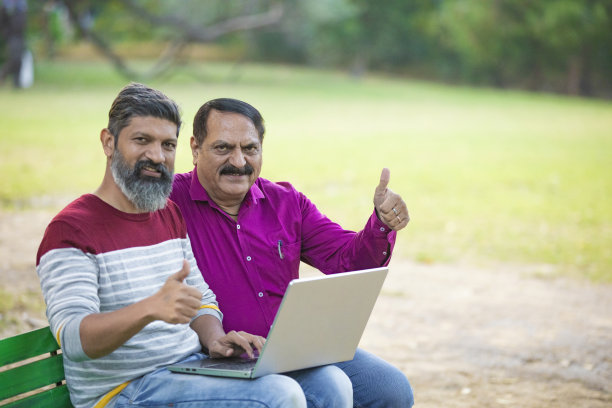 两个印度人在公园里用笔记本电脑拍照片。图片下载