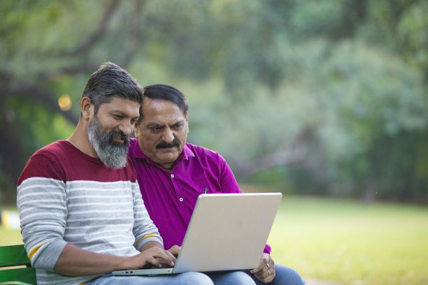 两个印度人在公园用笔记本电脑。图片下载