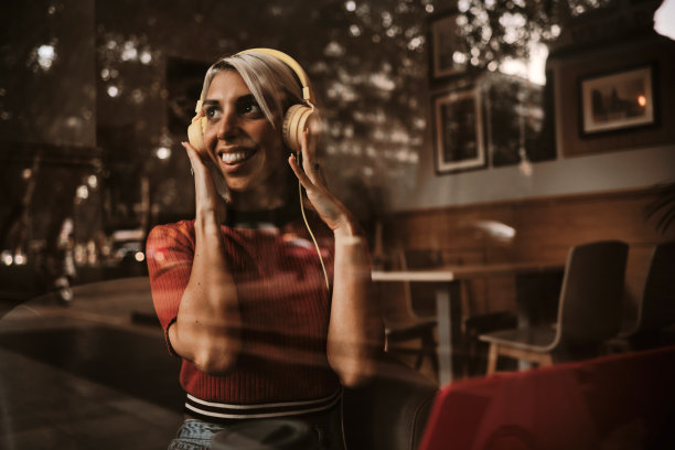 一名女子坐在咖啡店里，戴着耳机听音乐，面带微笑。图片下载