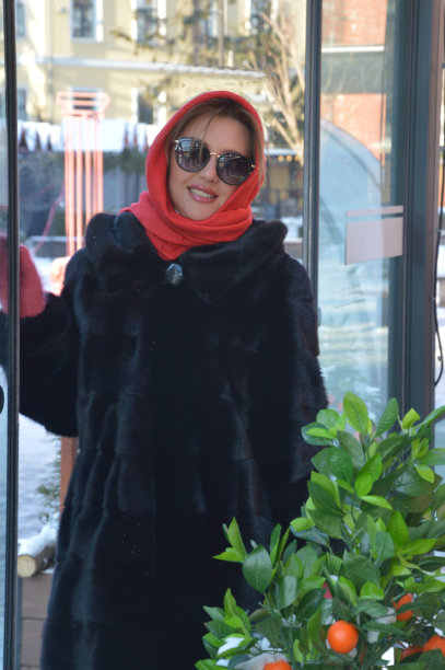 一个女孩的肖像在毛皮大衣，红色围巾和太阳镜在户外的冬天。年轻时尚的女人。图片下载