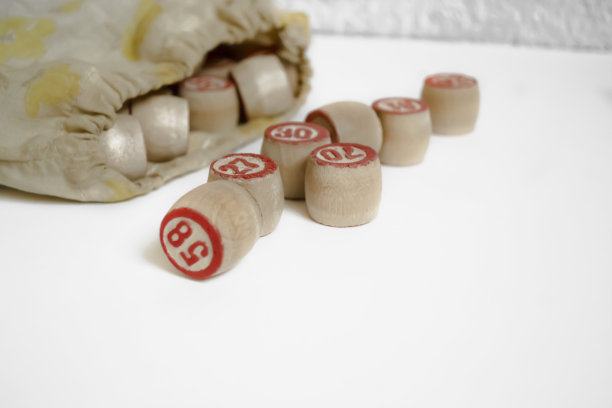 白色背景上的宾果桶。一种用木头做成数字的棋盘游戏的元素。一桶桶的盘子从袋子里倒出来，准备玩乐透牌游戏。图片下载