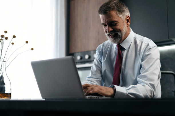 高级男子检查工作在厨房的笔记本电脑在家里图片下载