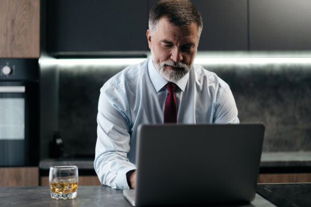 高级男子检查工作在厨房的笔记本电脑在家里图片下载