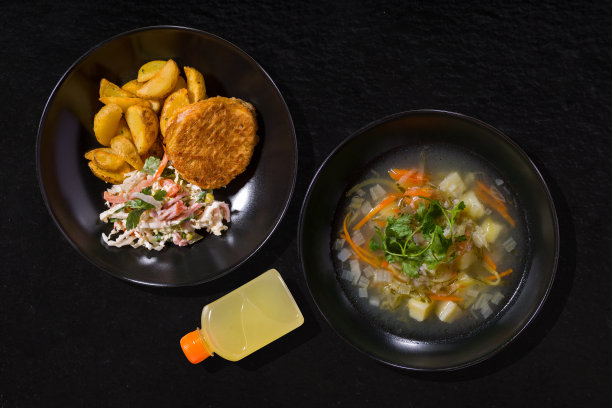 一盘土豆、胡萝卜、欧芹、洋葱汤，一盘土豆、鸡排和沙拉，配上胡椒、卷心菜、豌豆、蛋黄酱、香肠、欧芹和一瓶白色酱汁，背景是黑色的石头图片下载