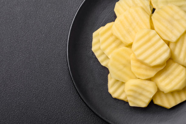 新鲜的土豆切成片放在黑色的陶瓷盘子上图片下载