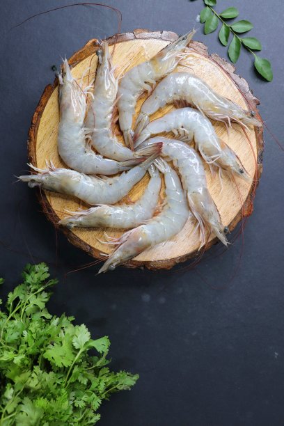 新鲜的虾或生的白虾放在木砧板上，配上香菜和咖喱叶。在后台复制空间。图片下载