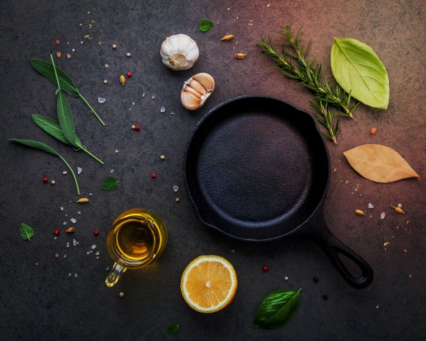 空旧铸铁炉料在黑色的石头背景。制作牛排概念的材料复制空间。各种草药和调味料迷迭香，鼠尾草，月桂叶，罗勒，大蒜和胡椒。图片下载