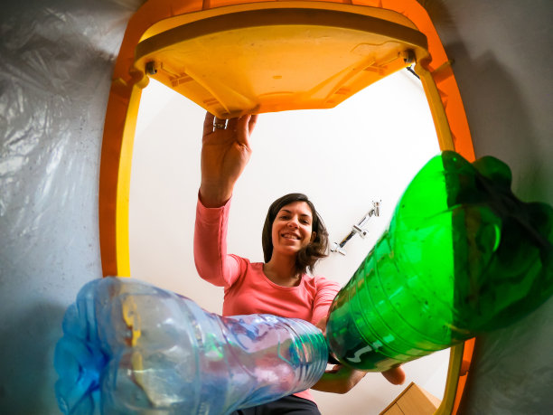 一位年轻女子将塑料瓶放入回收箱图片下载