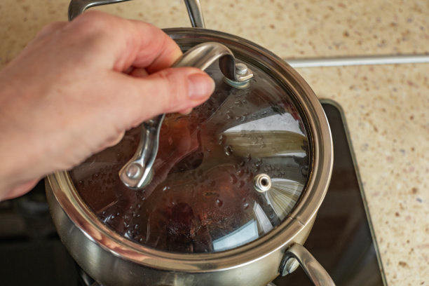煤气家用炉，红甜菜在一个透明玻璃盖的不锈钢炖锅里煮。女人用手盖上锅盖。烹饪健康食物的概念图片下载