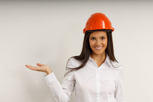 戴着橙色建筑头盔的漂亮模特。肖像快乐的微笑黑发女孩长头发，穿着白色的办公室衬衫。工作室拍摄的年轻女商人孤立的白色背景图片下载
