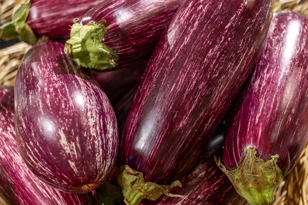 市场柜台上的柳条篮子里有紫色条纹的茄子。商店里的新鲜蔬菜。有涂鸦的紫茄子。特写镜头图片下载