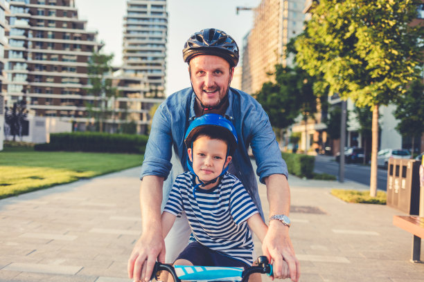 小男孩和他的父亲在公园边玩边学骑自行车。微笑的父亲教儿子在大自然中骑自行车。图片下载