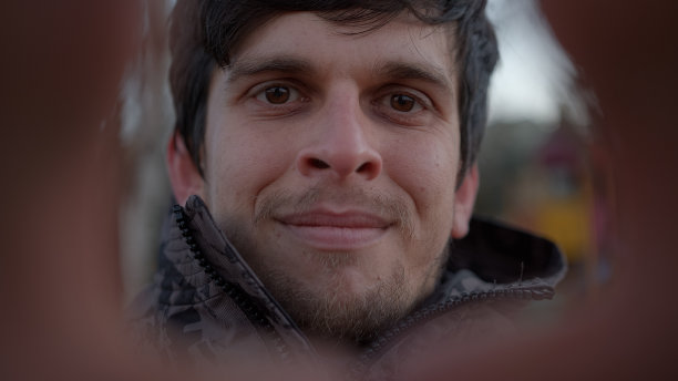 在户外，穿着夹克的迷人年轻人做着心形手势，对着镜头微笑图片下载