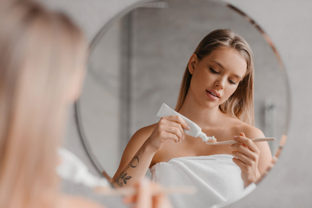 年轻女士早上刷牙，在牙刷上涂牙膏，站在浴室的镜子前图片下载