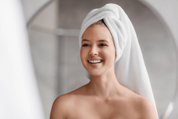美容护肤。女人看着镜子里的自己，微笑着，在浴室里做早上的美容例行公事图片下载