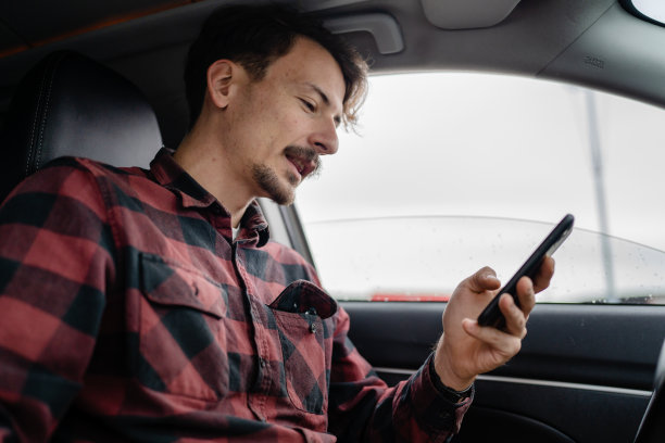 一个留着八字胡的白人男子坐在车里用手机图片下载