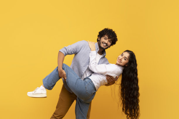在浪漫的约会中一起跳舞。快乐的印度男人和女人拥抱，对着黄色背景的相机微笑图片下载