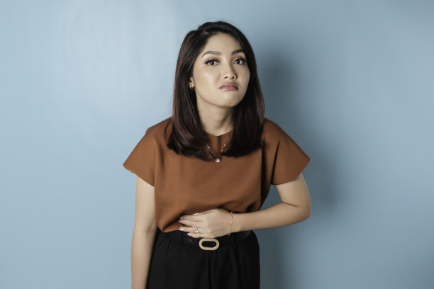 照片上年轻的生病的生病的女人手在胃上遭受疼痛隔离在蓝色背景图片下载