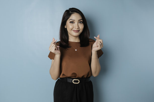 穿着棕色衬衫的迷人年轻亚洲女性感到快乐，浪漫的心形手势表达了温柔的感情图片下载