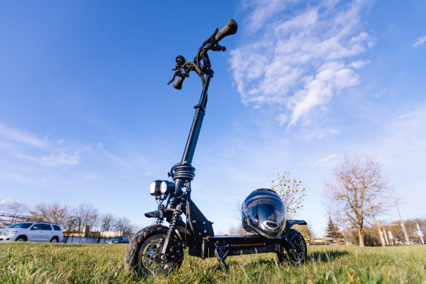 户外一辆黑色电动踏板车的照片。在建筑附近的绿色草地上骑滑板车。甲板上有防护头盔。生态交通概念摄影，生活方式摄影图片下载