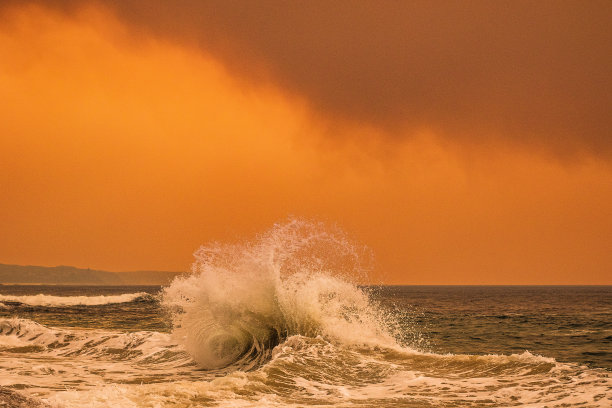海浪在沿海丛林大火产生的橙色烟雾下飞溅图片下载