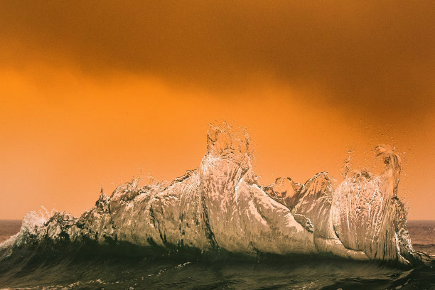 海浪在沿海丛林大火产生的橙色烟雾下飞溅图片下载