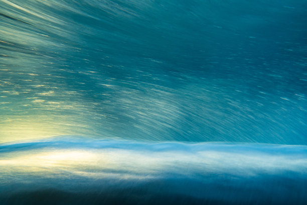 一种抽象的艺术场景，一个波浪在戏剧性的金色光线下在水下破碎图片下载