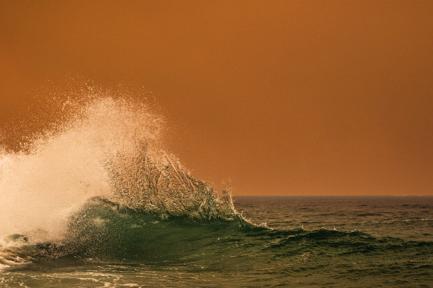 海浪在沿海丛林大火产生的橙色烟雾下飞溅图片下载