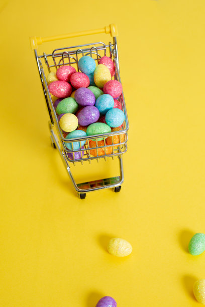 复活节快乐。购物车与彩色闪闪发光的复活节彩蛋在黄色的背景。俯视图图片下载