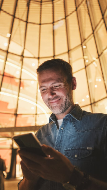 特写，中年男子晚上站在商业中心旁边使用手机图片下载