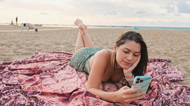 年轻微笑的女子在海滩上放松，使用手机图片下载