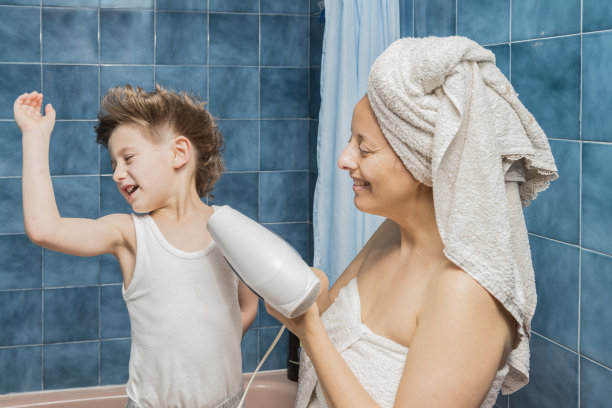 一个女人用吹风机吹孩子的头发。图片下载