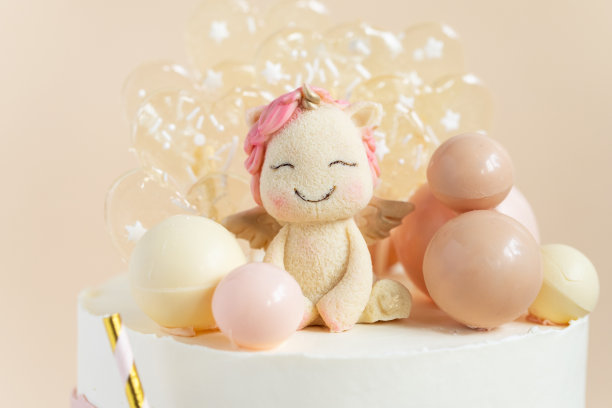 一个女孩的生日蛋糕，粉红色粉彩奶油奶酪糖霜装饰独角兽形象，巧克力球和焦糖在米色的背景。图片下载