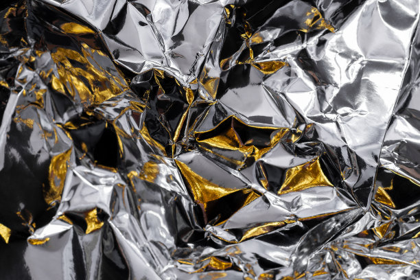 皱巴巴的银箔与金色和黑色的阴影。金属背景图片下载