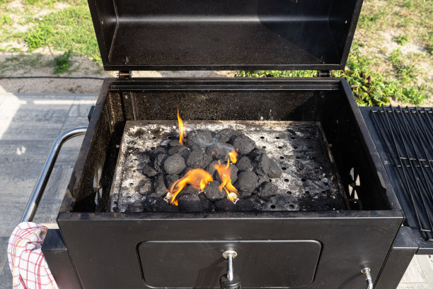 站在家里的花园，用烧烤打火机，用木炭和白色的火种点燃家庭烧烤架。图片下载