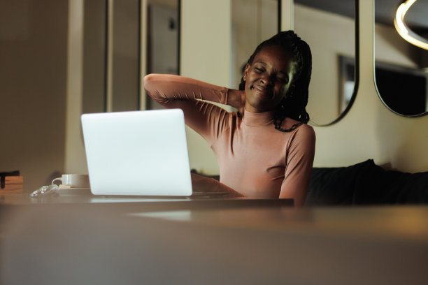 焦虑和疲劳生病的混血女商人，抱着脖子，感觉疼痛，在咖啡馆使用笔记本电脑。姿势不对，脊柱侧弯图片下载