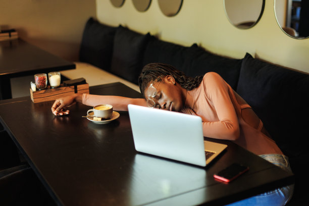 疲惫的多文化黑人美国女人在眼镜，躺在桌子上打瞌睡在网吧的笔记本电脑上喝咖啡图片下载