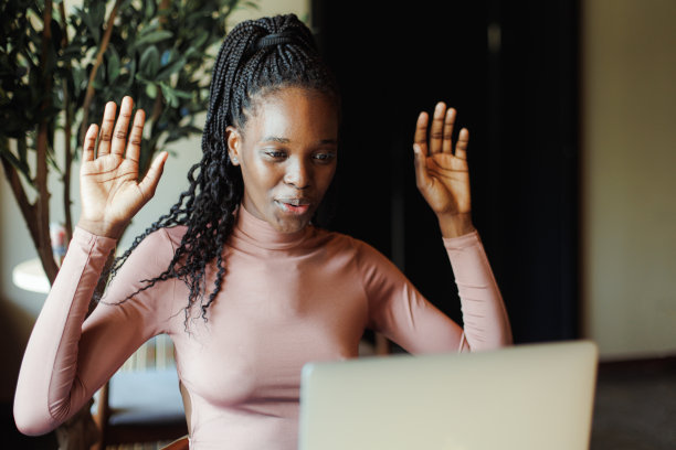 年轻兴奋的非裔美国妇女的肖像坐在桌子旁的咖啡馆笔记本电脑，举手，表示胜利。图片下载