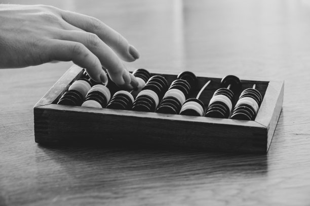 老式木算盘上的数钱木桌和一个女人的手在算盘上数钱，黑白照片图片下载