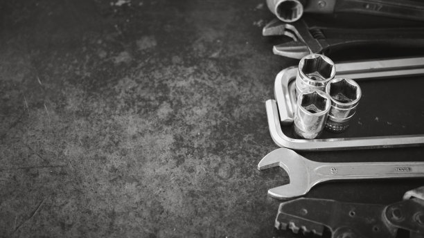 手动工具包括扳手、钳子、套筒扳手，放置在旧钢板背景上。图片下载