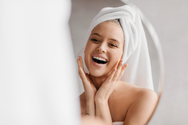 兴奋的年轻女士触摸她的脸，而看着镜子在浴室，漂亮的女人微笑着反思图片下载