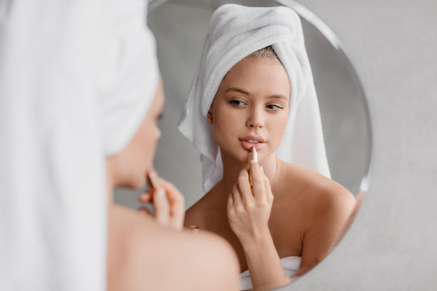 日常美容程序。漂亮的年轻女子涂口红，看着镜子，使用天然装饰性化妆品图片下载