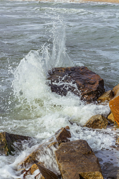 海浪的镜头。水花溅到石头上。海浪在岩石间翻腾。潮水的背景。图片下载