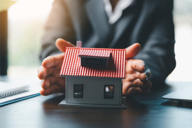 女性拯救有屋顶的小房子。房屋和不动产的概念财产保险。近距离的手庇护现代房屋图片下载