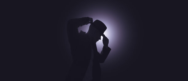 一个戴帽子的男人的剪影。背景中有明亮的灯光图片下载